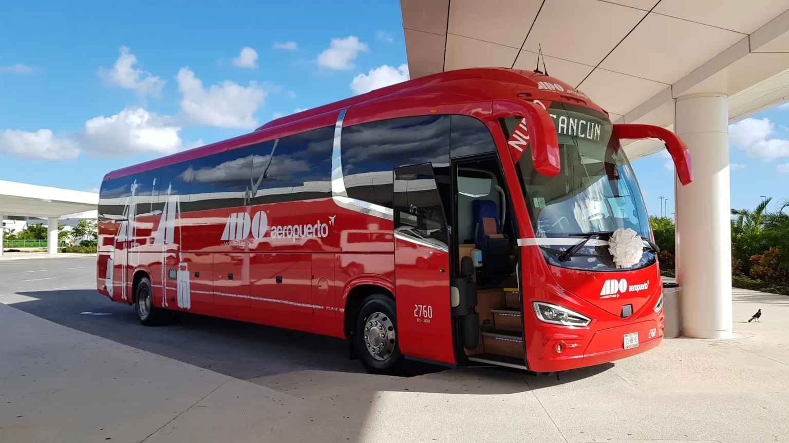 A modern red ADO coach at a terminal