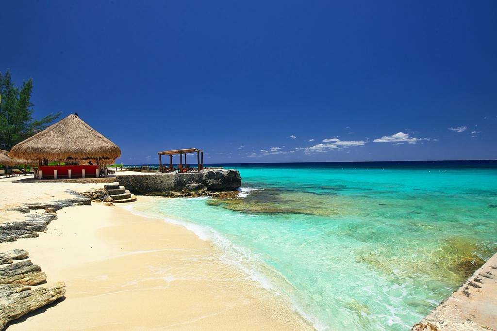 A palapa beside a rocky shoreline on Cozumel, with vivid turquoise water over a shallow reef
