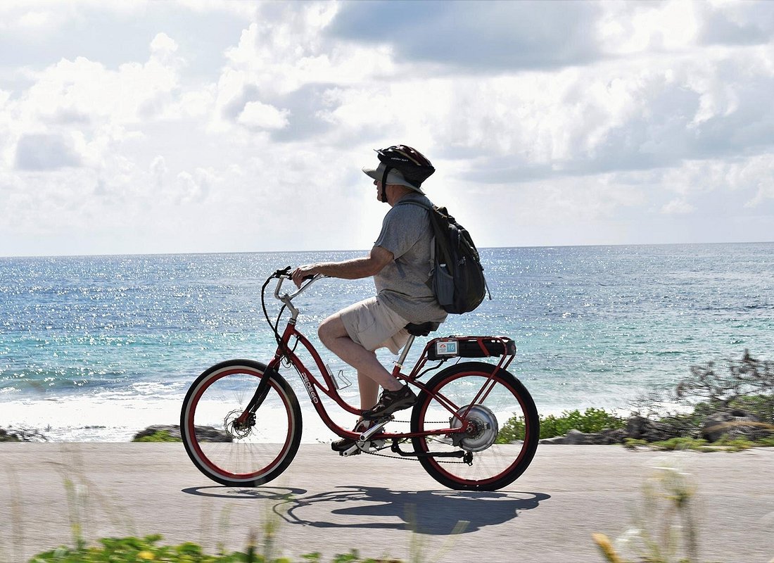 A cyclist riding a beach cruiser along a paved coastal path beside the turquoise Caribbean