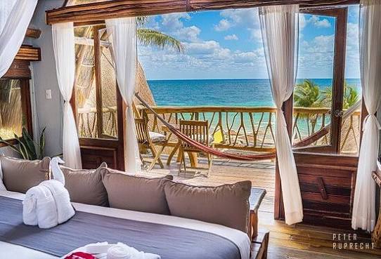 A beachfront room at Ahau Tulum opening to a private deck with a hammock and sea view