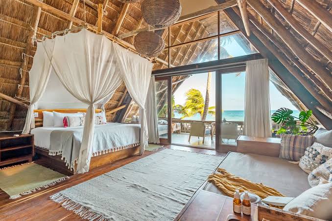 A soaring thatched A-frame loft bedroom with a canopy bed and ocean view at Ahau Tulum