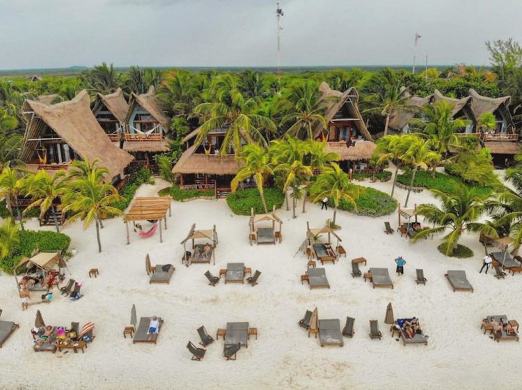 Aerial of Ahau Tulum's thatched A-frame cabañas and beach loungers scattered along white sand under palms