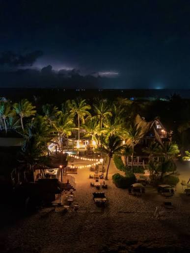 Ahau Tulum's beach glowing with string lights at night as distant lightning flashes over the sea