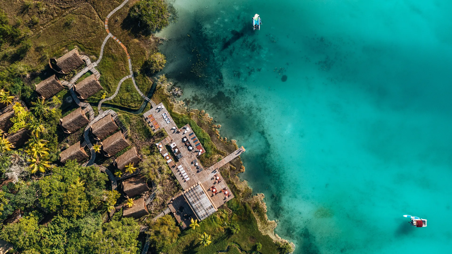 Aerial of Our Habitas Bacalar's thatched casitas and decks along the vivid turquoise Bacalar lagoon