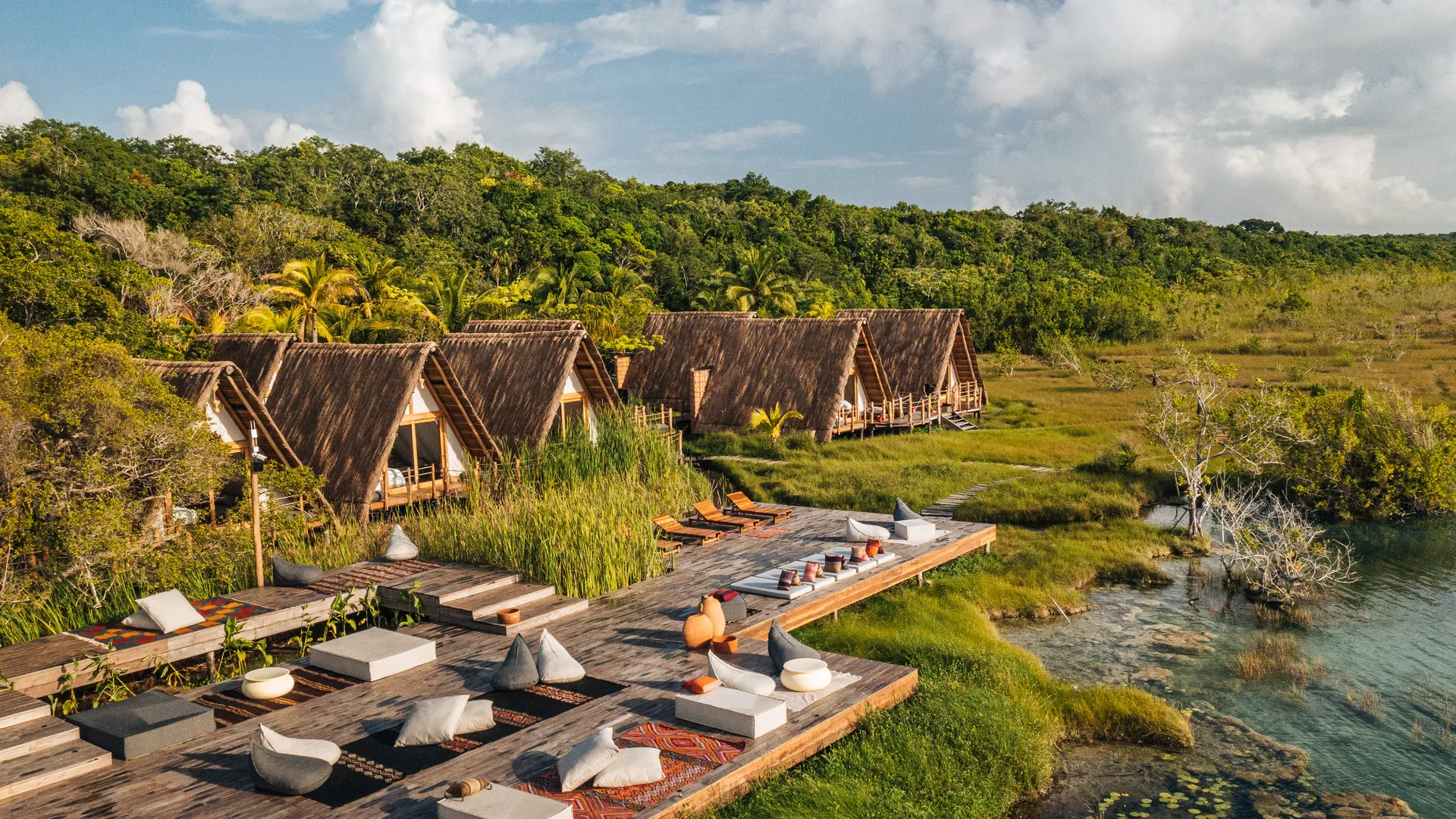 A-frame thatched casitas and cushioned lounge decks beside the Bacalar lagoon at golden hour