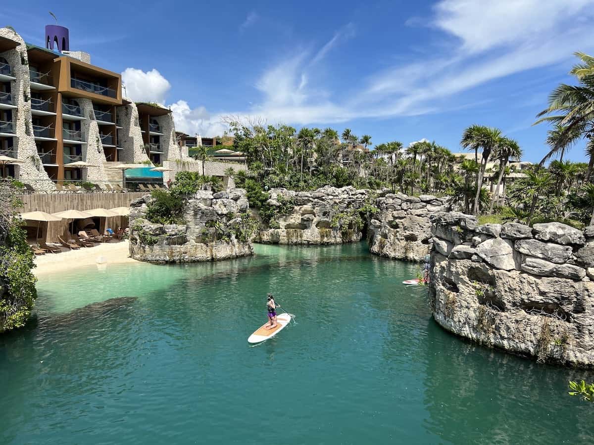 Guests paddleboarding along a rocky man-made river beneath the white-limestone towers of Hotel Xcaret Arte