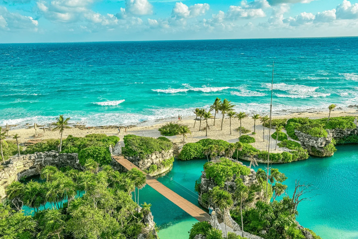 Aerial of Hotel Xcaret Arte's cenote pools and rope bridges leading out to a palm-lined Caribbean beach