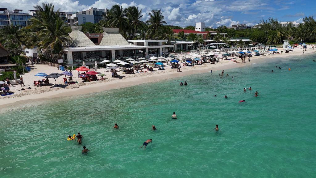 Mamita's Beach Club seen from the water at Playa Mamitas, with loungers, umbrellas and swimmers in turquoise water