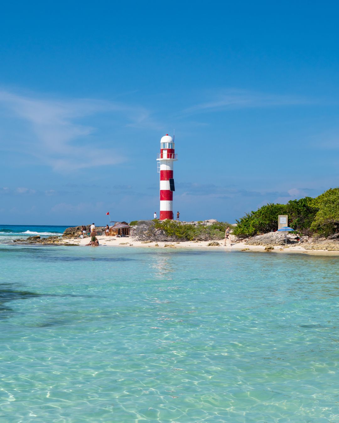 The red and white lighthouse of El Faro at Punta Cancún, above clear turquoise shallows