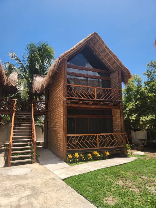 A two-storey house with a palapa roof built from sargassum-based bricks, with a wooden staircase and balcony