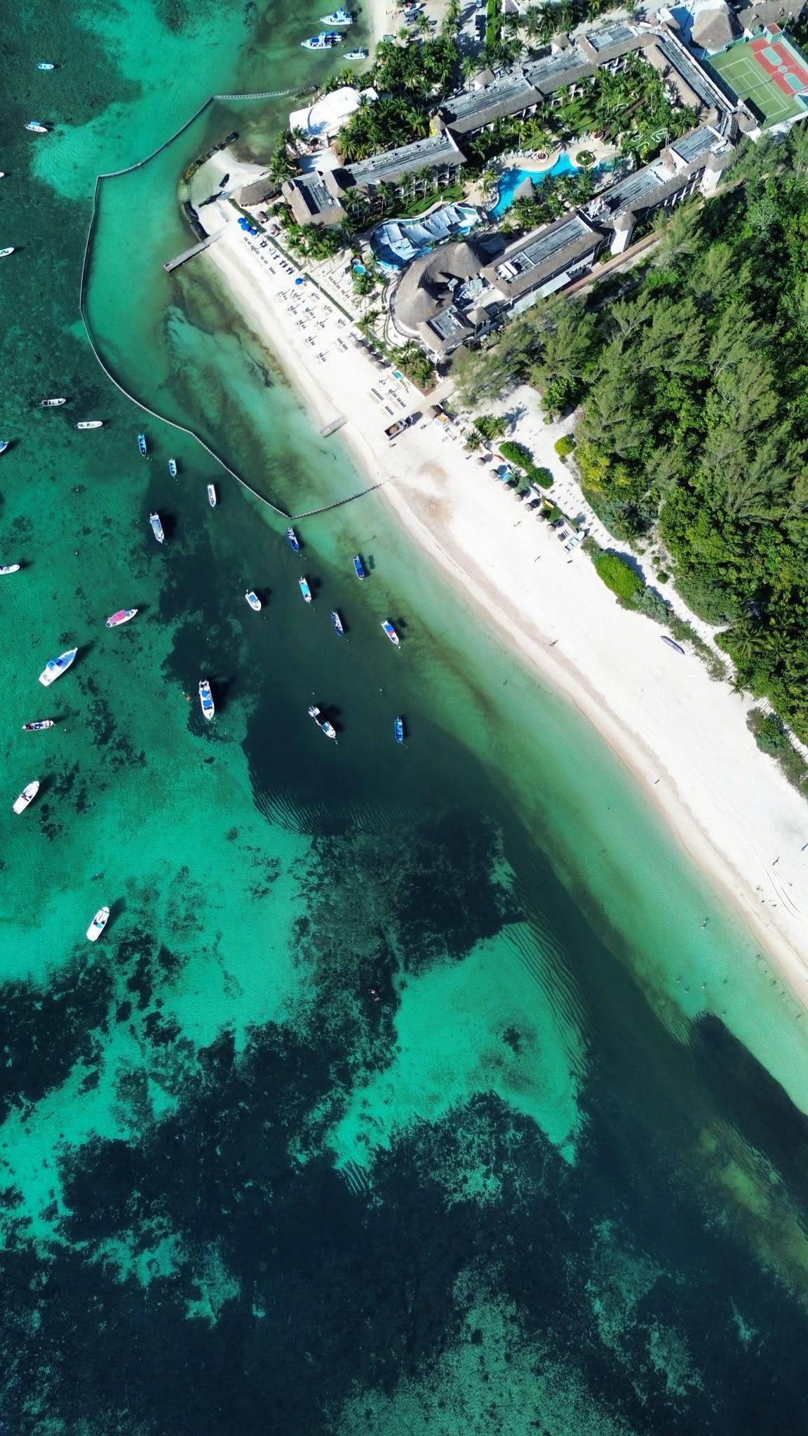 Aerial view of Playa Cisne at Calle 44 in Playa del Carmen on September 18, 2026, showing white sand, moored boats and clear green water inside the containment barrier